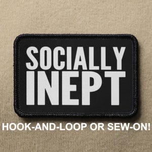 May include: Black patch with white text that reads "SOCIALLY INEPY" with a black border. The patch is labelled "HOOK-AND-LOOP OR SEW-ON!"