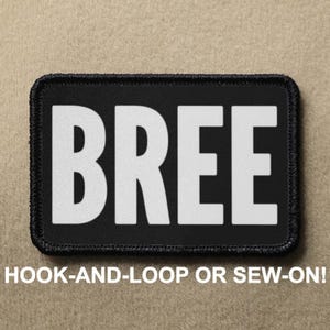 Pode incluir: Remendo preto com texto branco que diz "BREE". O remendo é para fixação de gancho e laço ou para costurar.