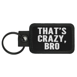 May include: Black rectangular keychain with the text "THAT'S CRAZY, BRO" in white. The keychain has a black fabric patch with rounded corners, a black metal ring, and a black fabric loop.