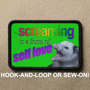 May include: A green patch with black stitching features a white opossum with its mouth open, and the text "screaming is a form of self love" in rainbow colours. The patch is labelled "HOOK-AND-LOOP OR SEW-ON!"