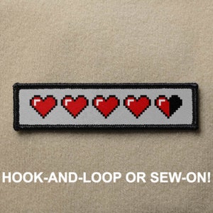 May include: A grey and black embroidered patch with five red pixelated hearts. The last heart is half black. The patch has hook-and-loop or sew-on backing. "HOOK-AND-LOOP OR SEW-ON!" is written in white text below the patch.