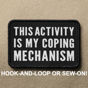 May include: Black rectangular patch with white text that reads "THIS ACTIVITY IS MY COPING MECHANISM." Below the text is "HOOK-AND-LOOP OR SEW-ON!" The patch has a black border and is on a tan background.