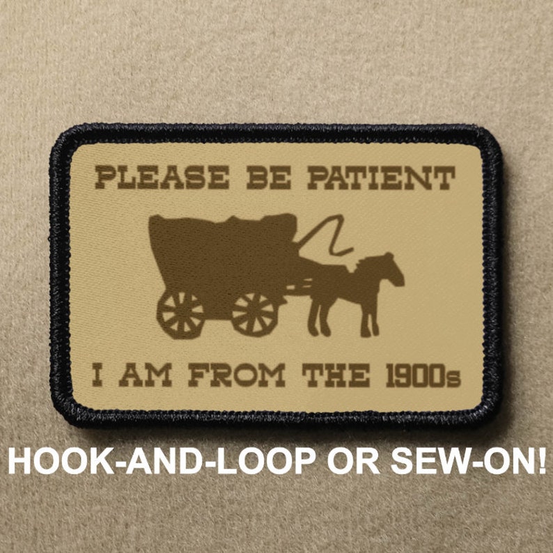 May include: A tan and brown embroidered patch with black stitching. The patch features a silhouette of a horse-drawn wagon with the text "PLEASE BE PATIENT I AM FROM THE 1900s". The patch is designed to be attached with hook-and-loop or sewn on.