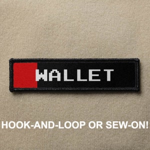 May include: Black and red patch with white text that reads "WALLET" in a pixelated font. The patch has hook-and-loop or sew-on backing.
