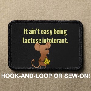Könnte beinhalten: Schwarz-weiß-Patch mit einer Comic-Maus, die ein Stück Käse hält. Der Text auf dem Patch lautet "It ain't easy being lactose intolerant."