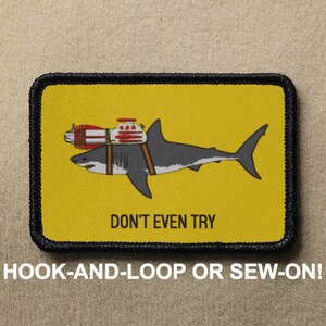 Op de afbeelding: Een gele patch met een zwarte rand heeft een cartoonillustratie van een haai met een raket op zijn rug. De tekst "DON'T EVEN TRY" staat onder de haai. De patch is ontworpen voor klittenband of om te naaien.