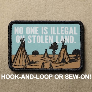 May include: Rectangular patch with a black border featuring a landscape scene with teepees and the text "NO ONE IS ILLEGAL ON STOLEN LAND." The bottom of the patch reads "HOOK-AND-LOOP OR SEW-ON!"