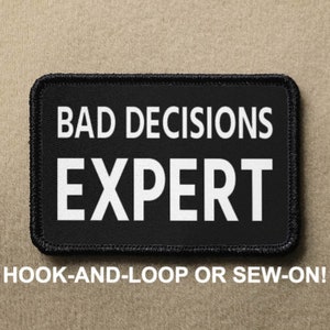 Könnte beinhalten: Schwarzer Patch mit weißem Text, der "BAD DECISIONS EXPERT" lautet. Der Patch ist für Klettverschluss oder zum Annähen.