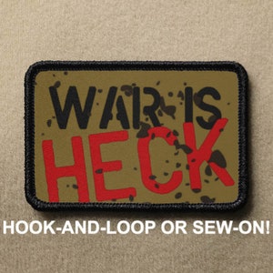 May include: A tan and black embroidered patch with the text "WAR IS HECK" in black and red lettering. The patch has a black border and a speckled background.