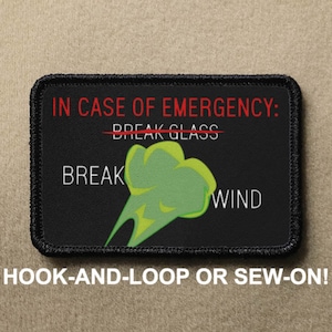 May include: Black and white patch with red text that says "IN CASE OF EMERGENCY: BREAK GLASS" with a line through the word "GLASS".  The word "BREAK" is written below the line and the word "WIND" is written to the right of a green cartoon cloud.  The text "HOOK-AND-LOOP OR SEW-ON!" is written below the patch.