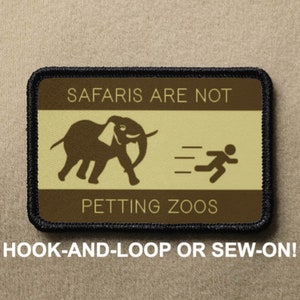 May include: A brown and black patch with white text that reads "SAFARIS ARE NOT PETTING ZOOS". The patch features a brown elephant and a running person in black. The patch is surrounded by a black border.