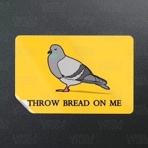 Puede incluir: Una pegatina amarilla con una paloma gris de dibujos animados y el texto "THROW BREAD ON ME".