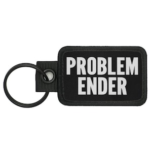 Könnte beinhalten: Schwarzer Schlüsselanhänger mit einem schwarzen rechteckigen Patch, auf dem "PROBLEM ENDER" in weißer Schrift steht.