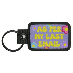 May include: A rectangular keychain with the text "AS PER MY LAST EMAIL" in yellow letters on a lavender background. The design includes colorful flower graphics. The keychain has a black ring and a black fabric loop.