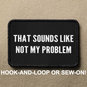 May include: Black patch with white text that reads "THAT SOUNDS LIKE NOT MY PROBLEM". The patch is for hook-and-loop or sew-on attachment.