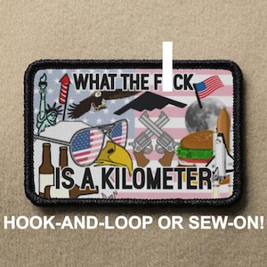 May include: A black and white patch with a pink background. The patch features a variety of images including a bald eagle, a fighter jet, a hamburger, a rocket ship, and a bottle of beer. The text on the patch reads "WHAT THE FOCK IS A KILOMETER".