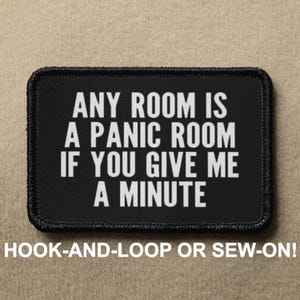 Peut inclure: Un patch noir avec du texte noir et blanc qui dit "ANY ROOM IS A PANIC ROOM IF YOU GIVE ME A MINUTE". Le patch a une bordure noire et est étiqueté "HOOK-AND-LOOP OR SEW-ON!"