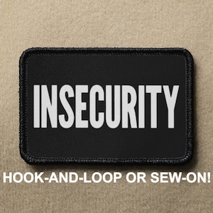 Può includere: Toppa nera con testo bianco che recita "INSECURITY". La toppa è progettata per essere fissata con velcro o cucita.