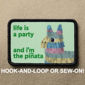 May include: Rectangular patch with a black border and a light green background. The patch features a colorful piñata illustration and the text "life is a party and I'm the piñata". The bottom of the patch reads "HOOK-AND-LOOP OR SEW-ON!"