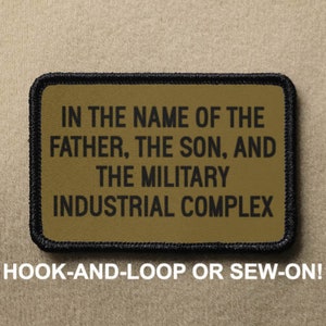 May include: A brown patch with black stitching and the text "IN THE NAME OF THE FATHER, THE SON, AND THE MILITARY INDUSTRIAL COMPLEX" in black. The patch is labeled "HOOK-AND-LOOP OR SEW-ON!"