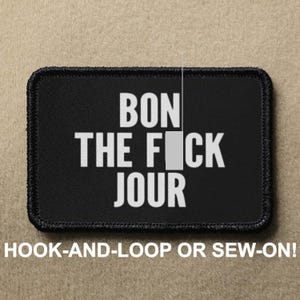 Peut inclure: Patch brodée noir et blanc avec le texte "BON THE FICK JOUR" sur un fond noir. Le patch est conçu pour une fixation par scratch ou par couture.