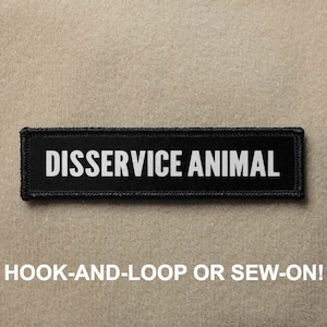 Pode incluir: Etiqueta preta com texto branco que diz "DISSERVICE ANIMAL". A etiqueta é projetada para ser fixada com velcro ou costurada.
