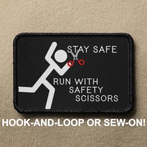 May include: Black and white patch with a stick figure running with safety scissors. The text reads "Stay Safe Run With Safety Scissors". The patch is for hook-and-loop or sew-on.