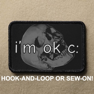 Puede incluir: Parche bordado en blanco y negro con una calavera y el texto "i'm ok c:". El parche tiene un borde negro y está diseñado para ser fijado con velcro o cosido.