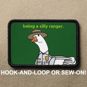 May include: A green and black embroidered patch with a cartoon goose wearing a ranger hat and uniform. The text "being a silly ranger." is above the goose. The patch has a hook and loop backing.
