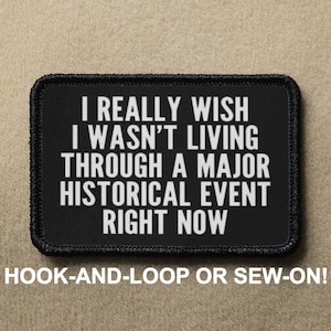 May include: Black rectangular patch with white text: "I REALLY WISH I WASN'T LIVING THROUGH A MAJOR HISTORICAL EVENT RIGHT NOW." The text "HOOK-AND-LOOP OR SEW-ON!" is below the patch. The patch has a black border and is on a tan background.
