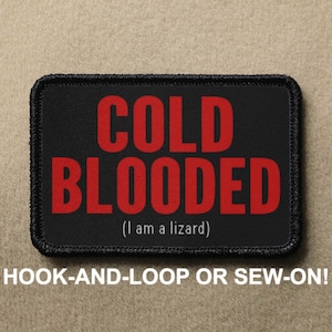 May include: Black patch with red text that reads "COLD BLOODED (I am a lizard)". The patch is for hook-and-loop or sew-on attachment.