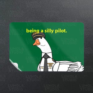 May include: A green sticker with a white goose wearing a pilot's hat and uniform. The text "being a silly pilot." is written in yellow letters.