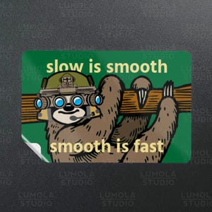 May include: A green sticker with a cartoon sloth wearing a camouflage helmet with night vision goggles. The sloth is holding a wooden branch. The text on the sticker reads "slow is smooth, smooth is fast".