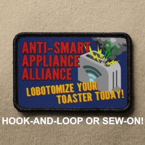 May include: A blue and black embroidered patch with the text "ANTI-SMART APPLIANCE ALLIANCE LOBOTOMIZE YOUR TOASTER TODAY!" and a cartoon image of a toaster with scissors cutting a wire. The patch is for hook-and-loop or sew-on attachment.