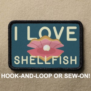 Puede incluir: Un parche azul y blanco con el texto "I LOVE SHELLFISH" y una concha rosa con una perla en su interior. El parche está rodeado por un borde negro.