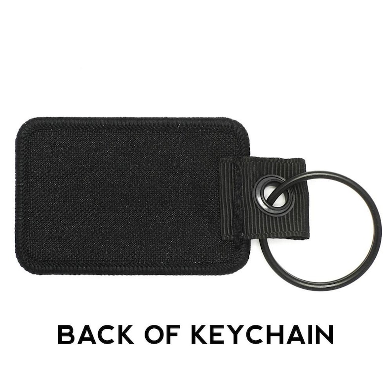 May include: Black fabric keychain with a black metal ring. The back of the keychain is blank.
