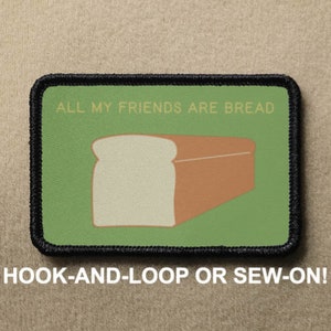 Könnte beinhalten: Ein grüner und schwarzer gestickter Aufnäher mit dem Text "ALL MY FRIENDS ARE BREAD" und einem Cartoon-Bild eines Laibes Weißbrots. Der Aufnäher ist so konzipiert, dass er mit Klettverschluss befestigt oder angenäht werden kann.