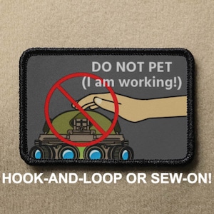 May include: A black and grey patch with a cartoon robot with a red circle and slash over it. The text on the patch reads "DO NOT PET (I am working!)" and "HOOK-AND-LOOP OR SEW-ON!"