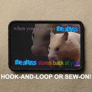 May include: A black and white patch featuring a picture of two hamsters. The text "when you stare into the abyss" is at the top of the patch. The text "the abyss stares back at you" is at the bottom of the patch. The patch is labelled "HOOK-AND-LOOP OR SEW-ON!"