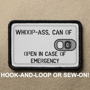May include: A white patch with black trim and the text "WHOOP-ASS, CAN OF" and "OPEN IN CASE OF EMERGENCY". There is a black and white graphic of a pull tab with the letter "C" on it. The text "HOOK-AND-LOOP OR SEW-ON!" is below the patch.