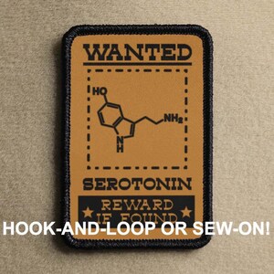 May include: A brown and black patch with a white outline. The patch has a wanted poster design with the text "WANTED" at the top and "SEROTONIN" below a chemical structure. The text "REWARD IF FOUND" is below the chemical structure. The bottom of the patch has the text "HOOK-AND-LOOP OR SEW-ON!"