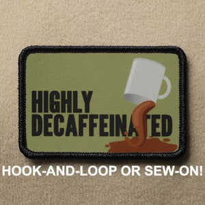 Puede incluir: Un parche bordado verde y negro con una taza de café blanca derramando café marrón. El texto en el parche dice "HIGHLY DECAFFEINATED". El parche es para sujetar con velcro o coser.