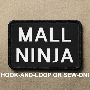 May include: Black patch with white text that reads "MALL NINJA". The patch has a black border and is designed to be attached with hook-and-loop or sewn on.