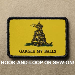 May include: A yellow patch with a black snake wrapped around a tower, with the text "GARGLE MY BALLS" below. The patch has a black border and is designed to be hooked or sewn onto clothing.