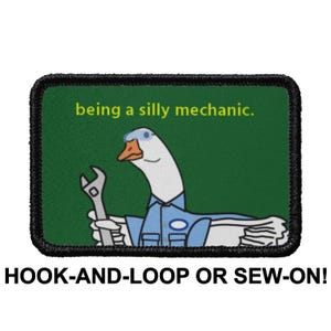 May include: A green and black embroidered patch with a white goose wearing a blue mechanic's uniform and holding a wrench. The text "being a silly mechanic." is written in yellow on the patch. The patch is for hook-and-loop or sew-on attachment.