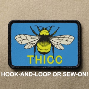 May include: A blue and white embroidered patch featuring a cartoon bumblebee and the word "THICC" in yellow lettering. The patch has a black border and is designed to be sewn or attached with hook and loop.
