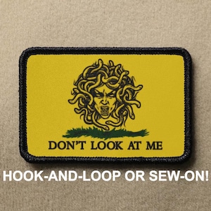 May include: A yellow patch with a black outline features a black and white illustration of Medusa, a mythical Greek figure with snakes for hair. The text "DON'T LOOK AT ME" is printed in black below the illustration. The patch is labeled "HOOK-AND-LOOP OR SEW-ON!"