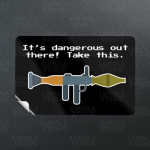 May include: A black and white sticker with a cartoon image of a rocket launcher and the text "It's dangerous out there! Take this."
