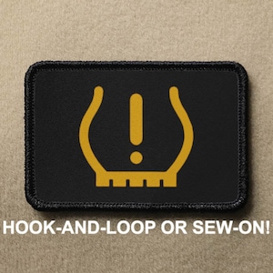 May include: Black patch with a yellow tyre pressure warning light symbol. The symbol has an exclamation mark inside of a tyre shape. The patch has black stitching around the edges. "HOOK-AND-LOOP OR SEW-ON!" is written in white text below the patch.