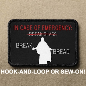 May include: Black patch with white text that reads "IN CASE OF EMERGENCY: BREAK GLASS" with a red line through "BREAK GLASS". Below the text is a white silhouette of a person with outstretched arms and the text "BREAK BREAD". The patch has black stitching around the edges and the text "HOOK-AND-LOOP OR SEW-ON!" is printed below the patch.
